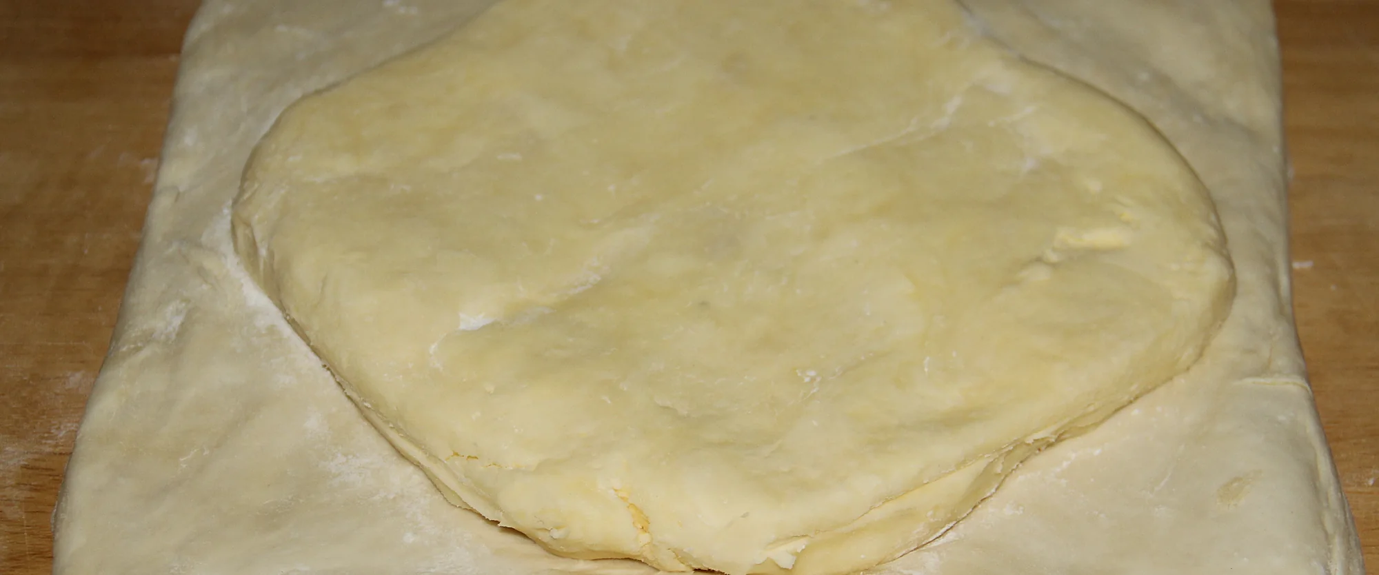 Une plaque de beurre posée sur une pâte étalée, sur une planche farinée, avant d'être enfermée.