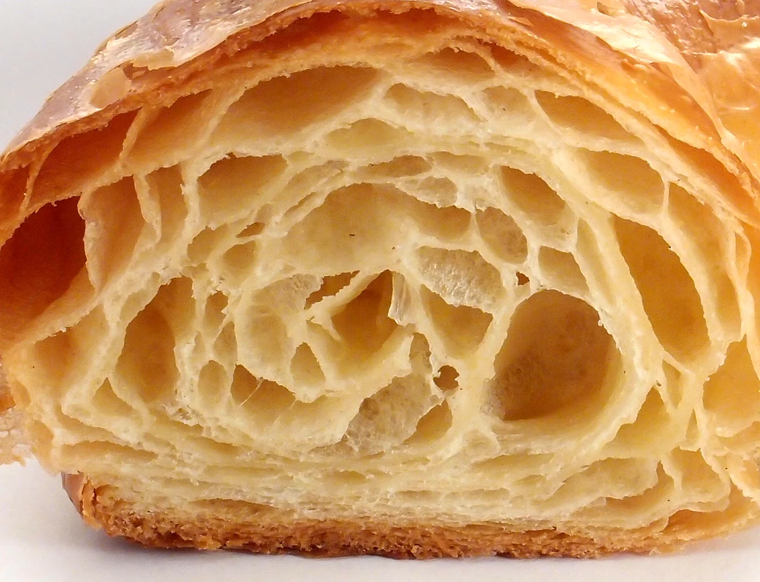 Le feuilletage d'un croissant coupé en deux, vu de très près : des dizaines de feuilles dorées et d'alvéoles.